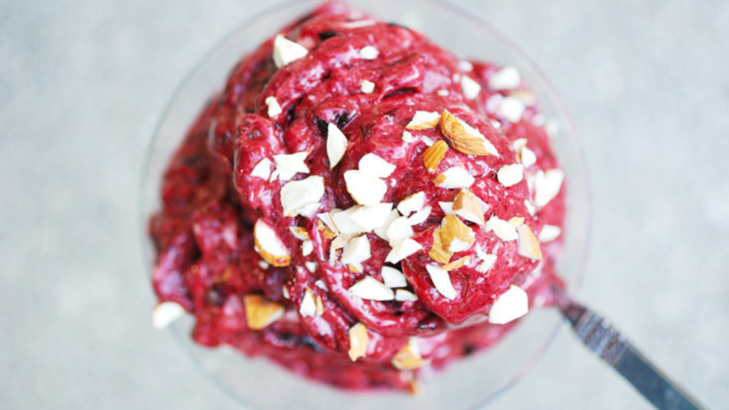 An overhead shot of a glass filled with cherry n'ice cream and topped with chopped almonds.