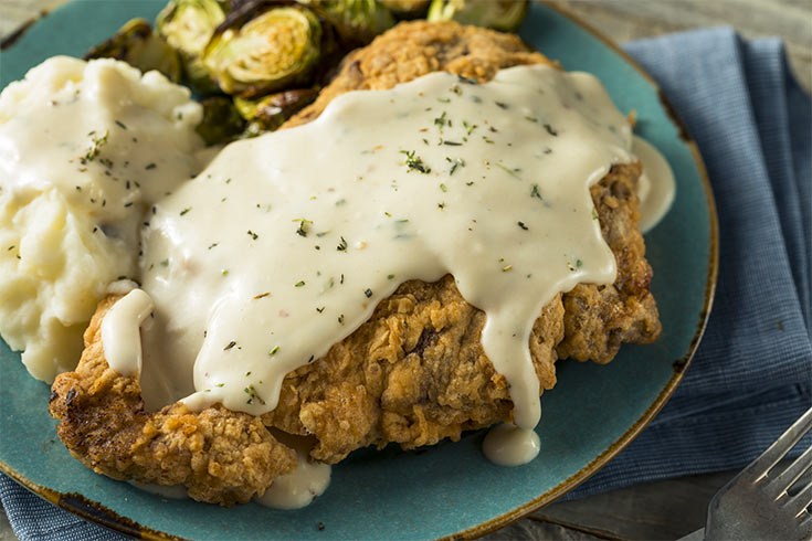 A chicken fried steak on a plate with mashed potatoes and brussels sprouts.