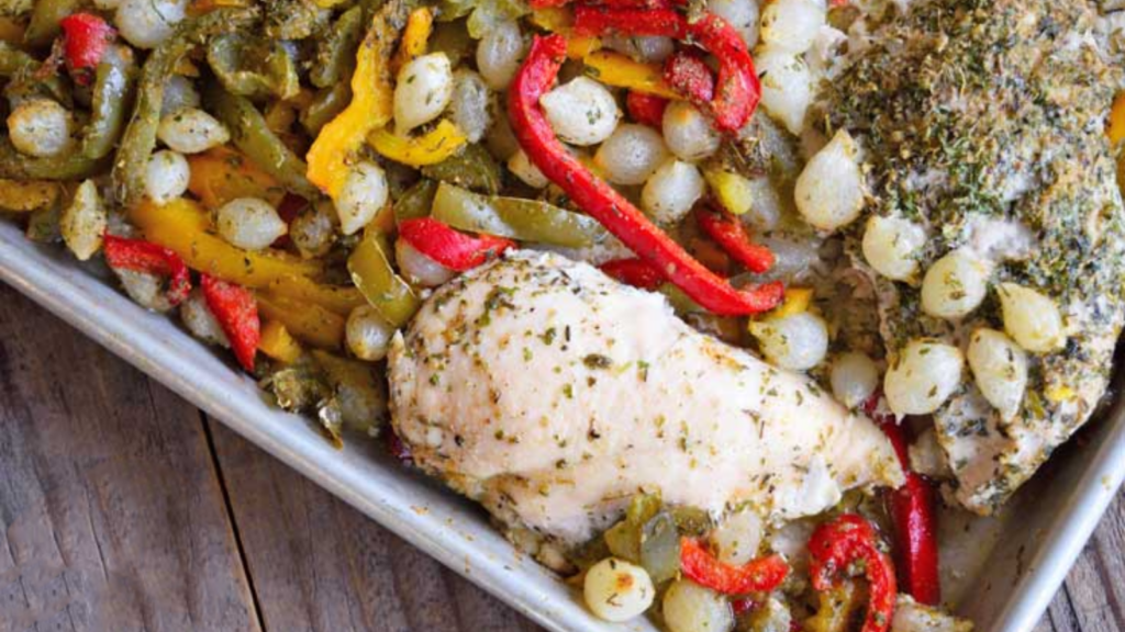 An overhead view of a sheet pan holding chicken and peppers with pearl onions.