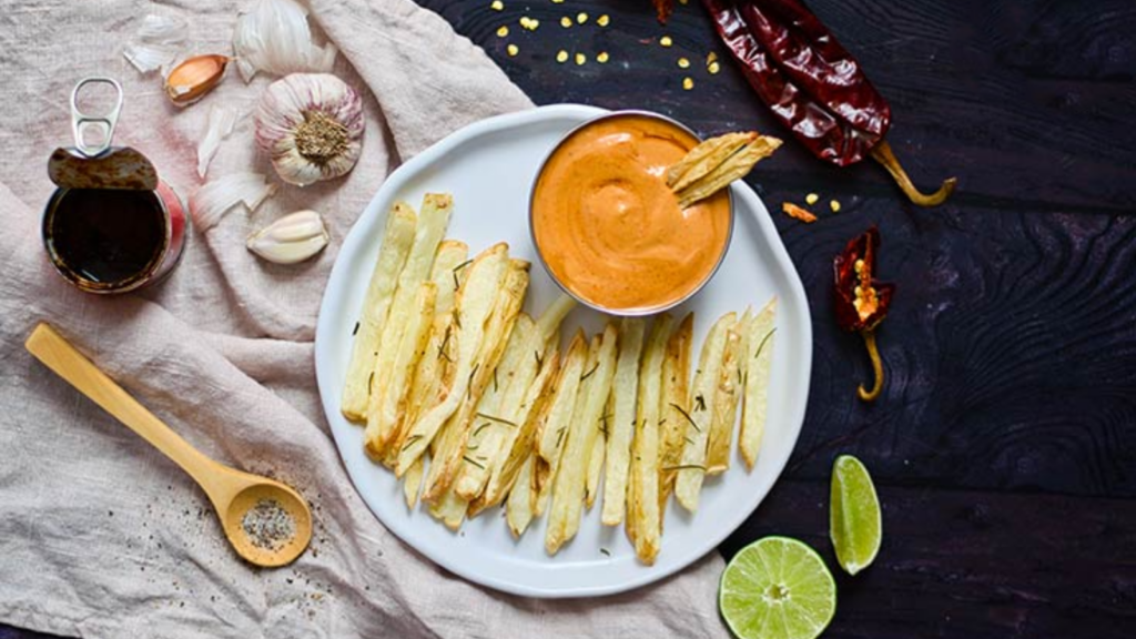 An overhead view of a small bowl of chipotle ailoli on a white plate with some french fries.