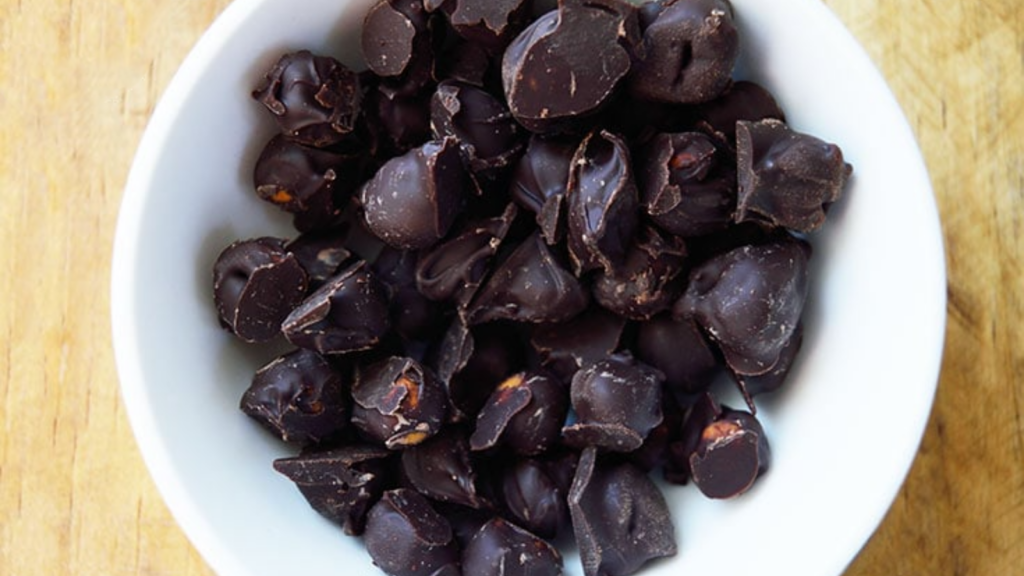 An overhead view of a white bowl holding chocolate covered chickpeas.