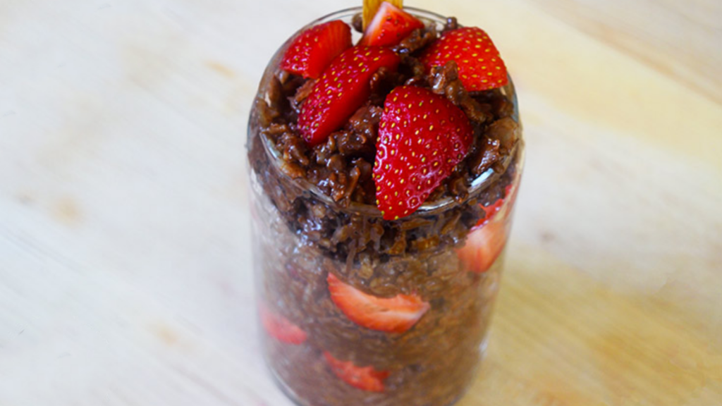 A clear glass is full of chocolate oatmeal and fresh, chopped strawberries.