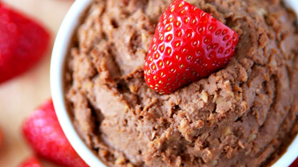 An overhead view of a white bowl full of chocolate peanut Butter Hummus and topped with a fresh strawberry.