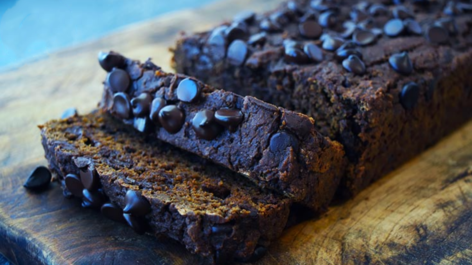 A loaf of chocolate pumpkin bread sits on a cutting board with two slices laying on top of it.