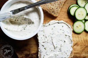 A slice of whole grain bread with chive cream cheese spread over it.