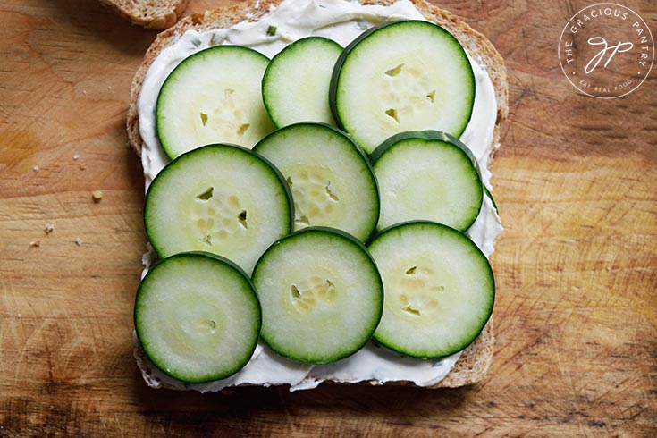 Cucumber slices covering the cream cheese on a single slice of whole grain bread.