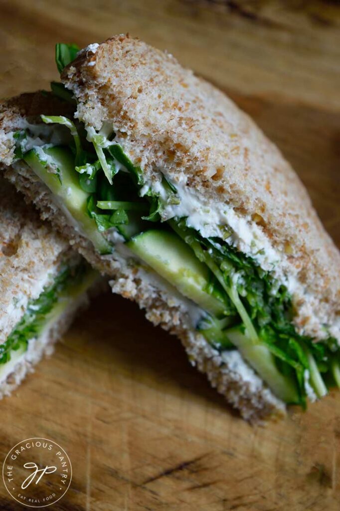 Half of a cucumber sandwich propped up on the other half on a wooden cutting board.