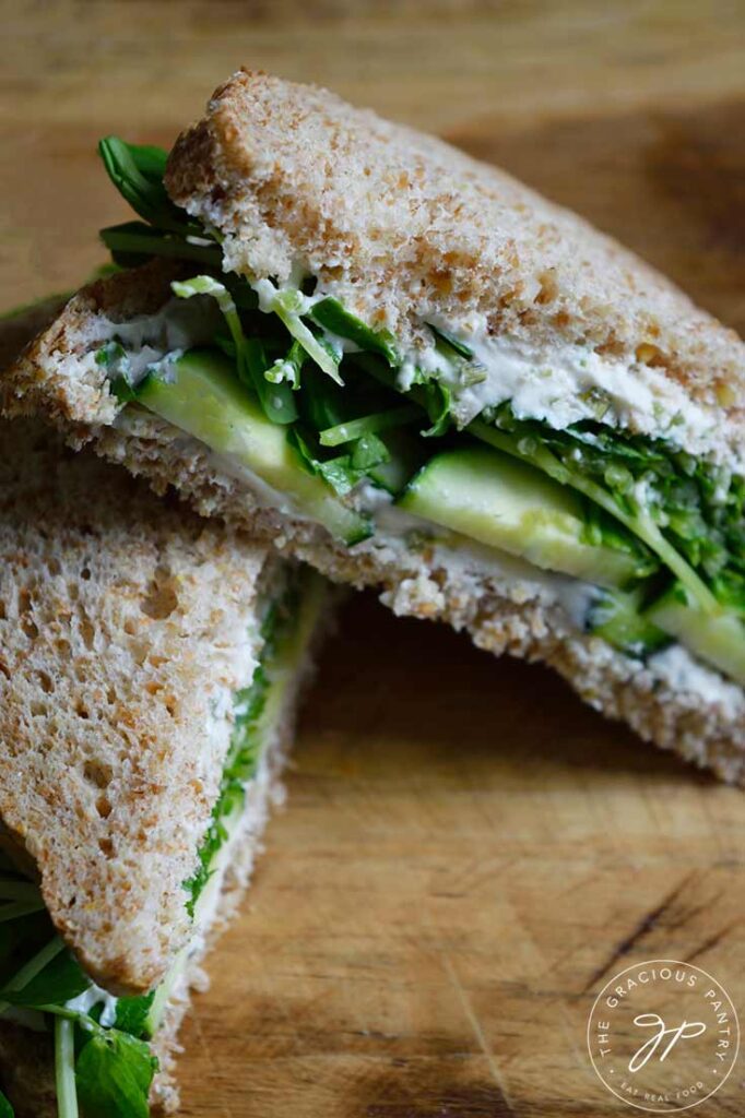 Two cut halves of a cucumber sandwich arranged on a wood cutting board.