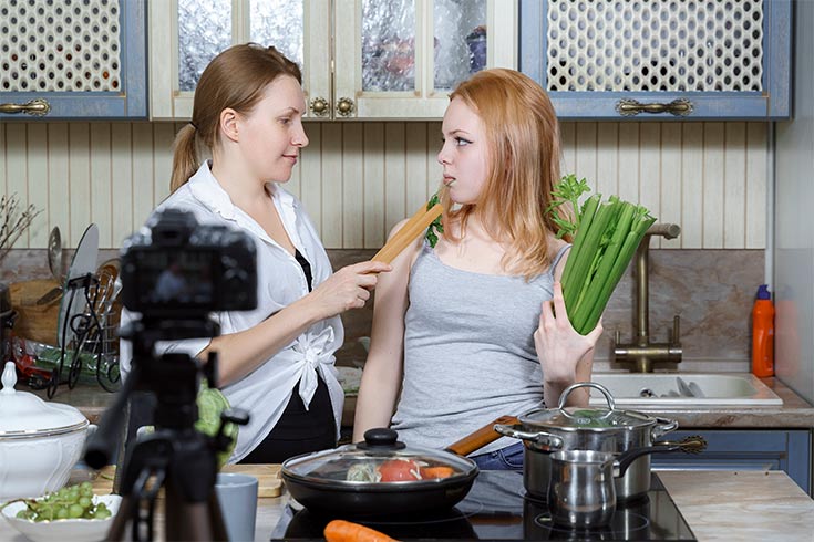 A woman trying to feed a young girl vegetables.