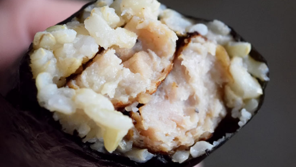 A closeup of a gimbap that has been broken in half to expose the hot dog and rice inside.