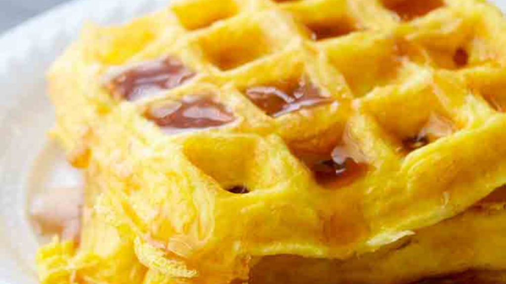 A closeup of a stack of two egg waffles with syrup on top.