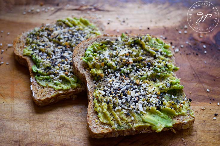Two slices of Everything Bagel Avocado Toast lay on a wooden surface.
