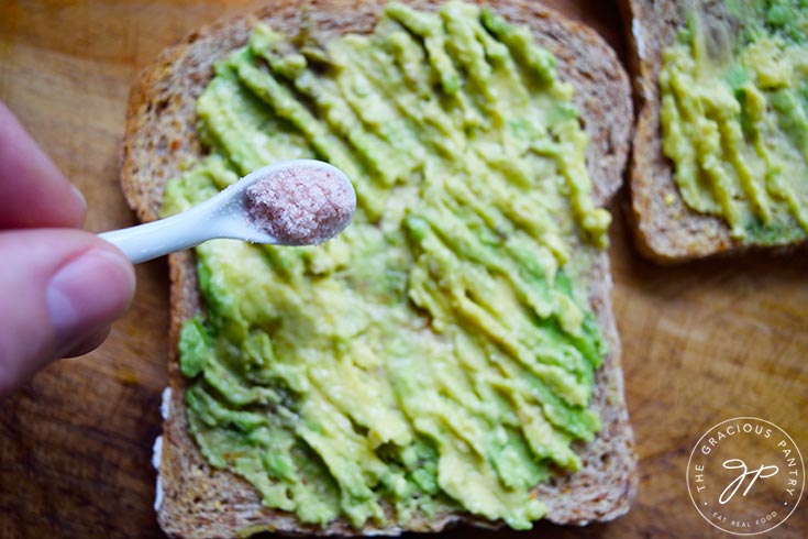 Sprinkling salt over the mashed avocado.