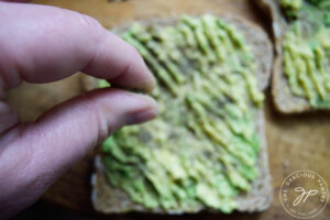 Sprinkling pepper over mashed avocado on toast.