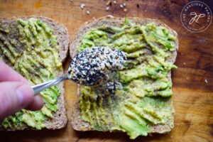 Sprinkling Everything Bagel Seasoning over mashed avocado on toast.