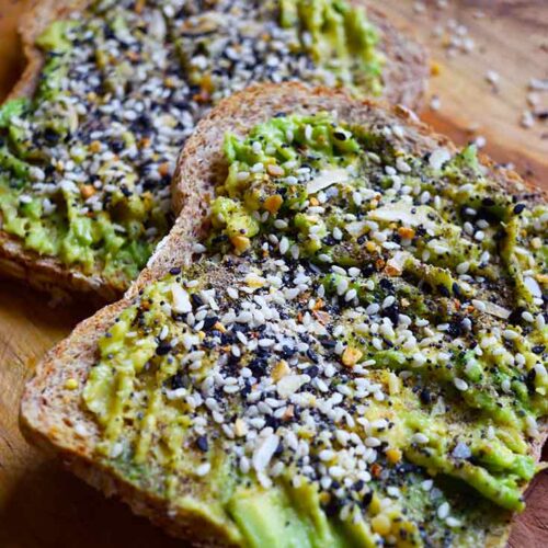 A front view of two slices of Everything Bagel Avocado Toast on a wooden surface.