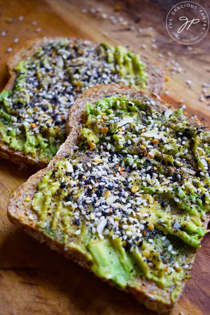 A front view of two slices of Everything Bagel Avocado Toast on a wooden surface.