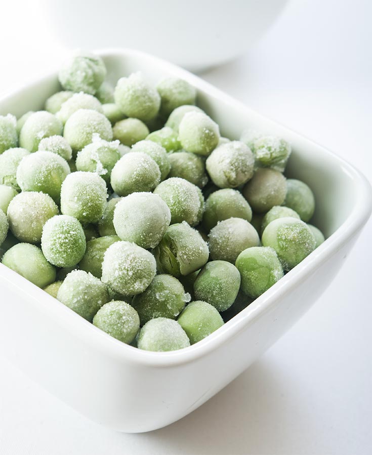 A white bowl of frozen peas.