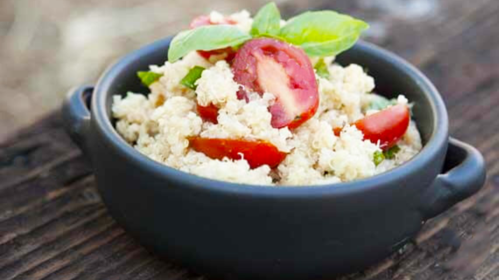 A black crock sits on a wood surface filled with garlic parmesan quinoa and garnished with fresh basil leaves.