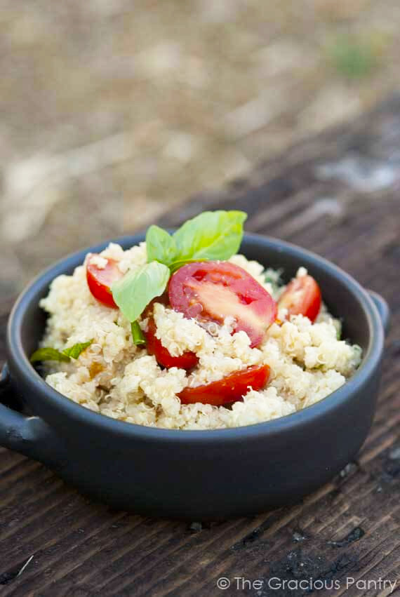 A vertical view of a black crock holding a serving of Garlic Parmesan Quinoa and garnished with fresh basil leaves.