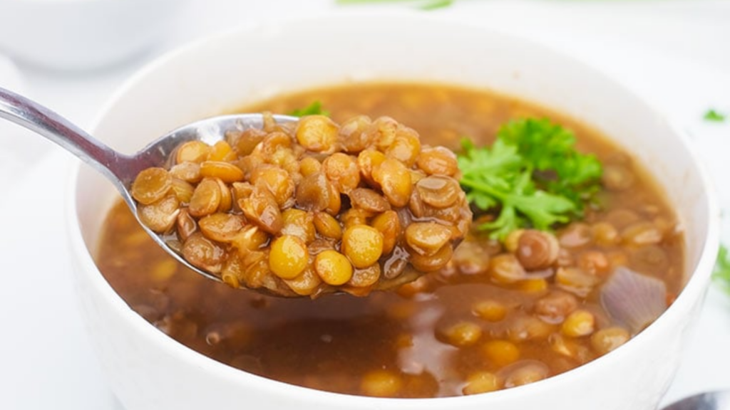 A spoon lifts some german lentil soup out of a white bowl.