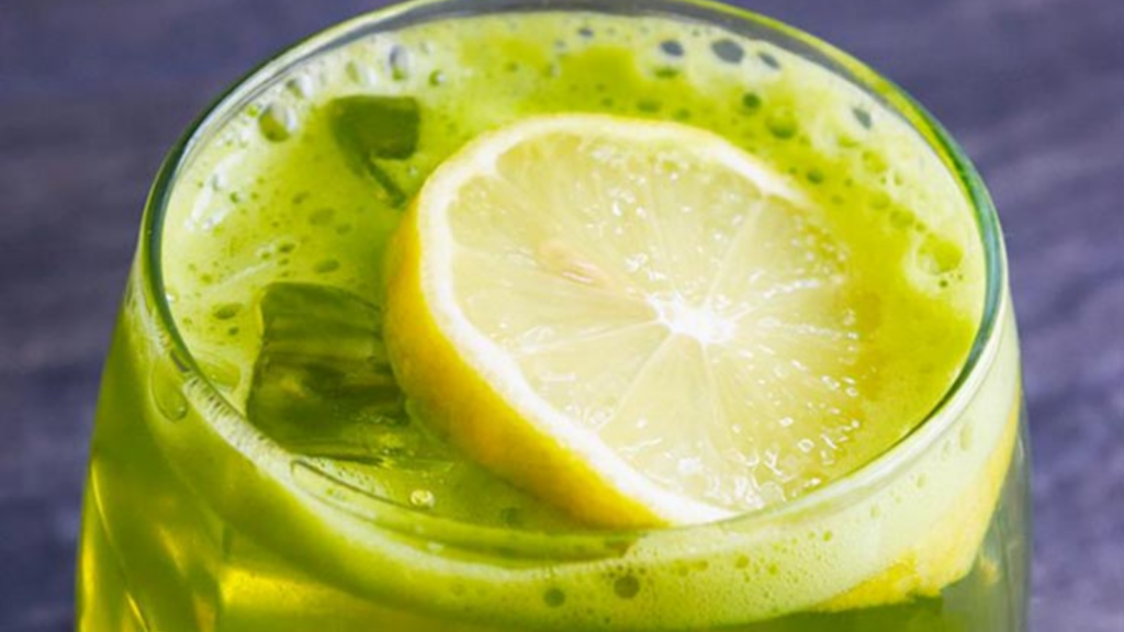 A closeup of a glass of green lemonade with a lemon slice on top.