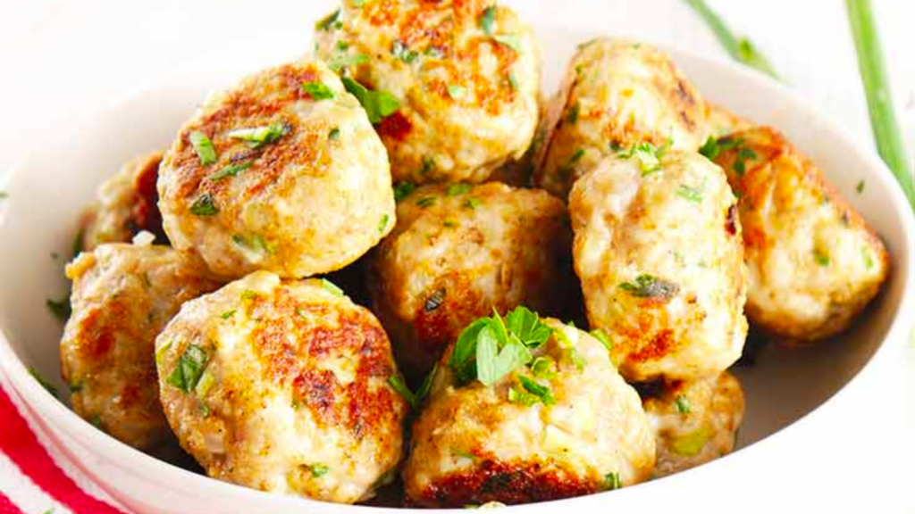 A white bowl filled with ground turkey meatballs and garnished with fresh parsley.