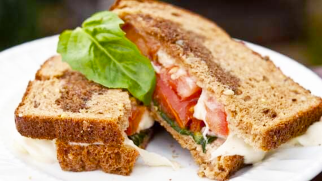 A grownup grilled cheese sandwich, cut in half, lays on a white plate.