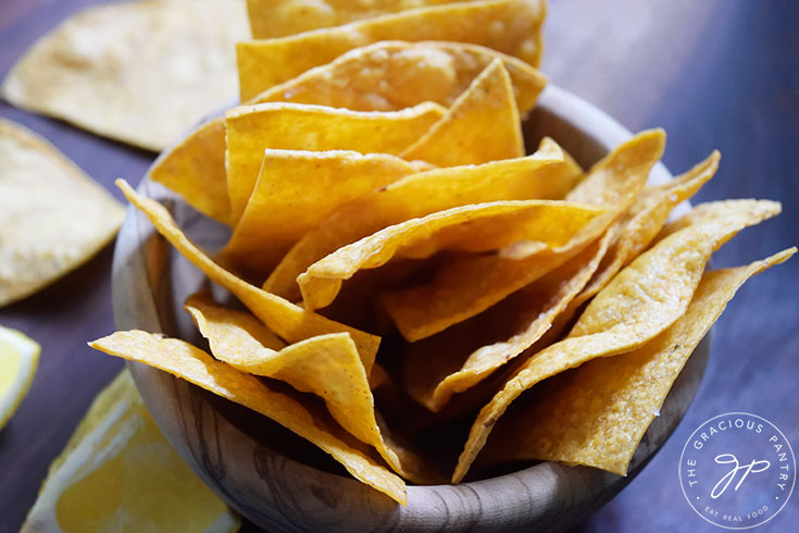 A wooden bowl holds a bowl full of homemade corn chips.