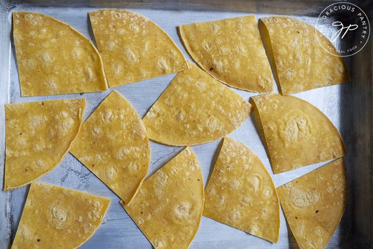 Quartered corn tortillas laying on a sheet pan.