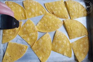 Spraying the unbaked corn chips with an oil sprayer.