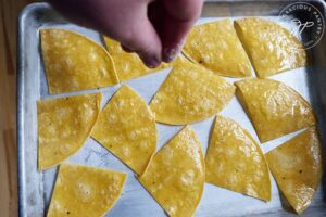 Sprinkling the oiled corn chips with salt.