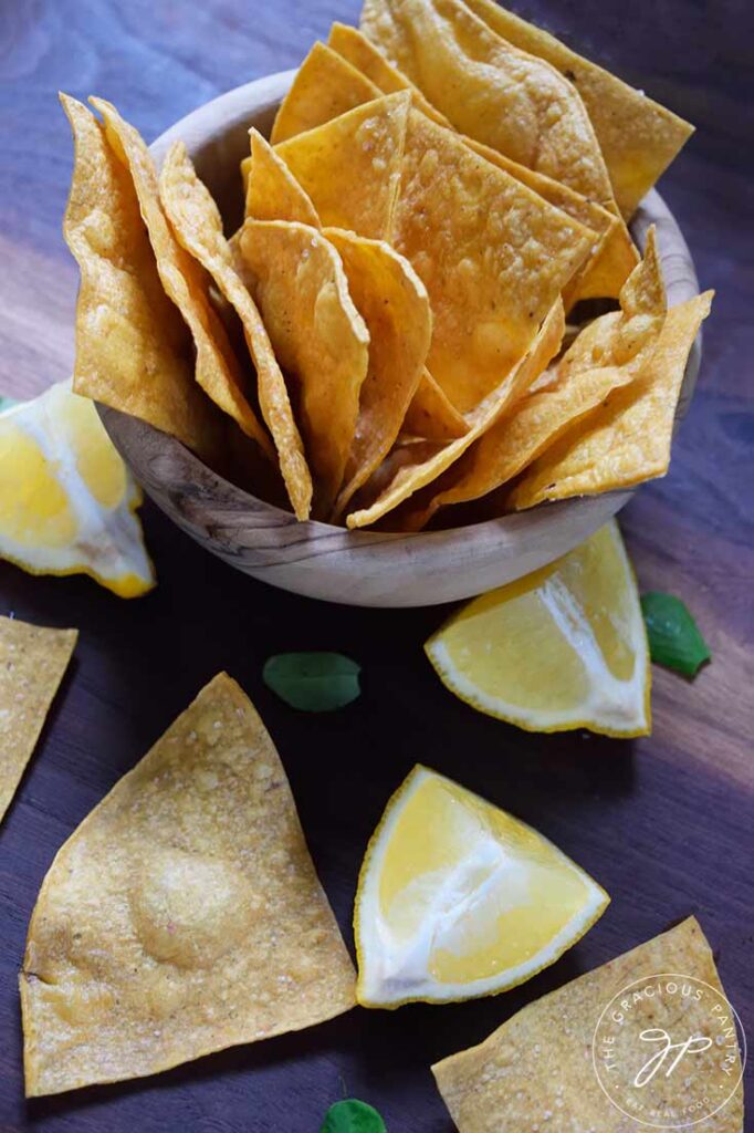 A wood bowl filled with Homemade Corn Chips with a few chips and lemon wedges scattered around the base.