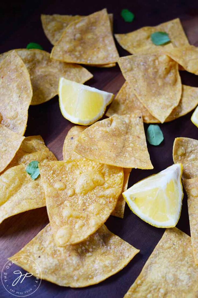 Homemade Corn Chips scattered on a cutting board with lemon wedges and chopped greens.