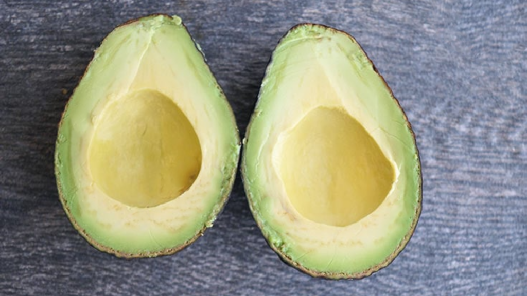 An overhead view of two avocado halves laying on a gray surface.