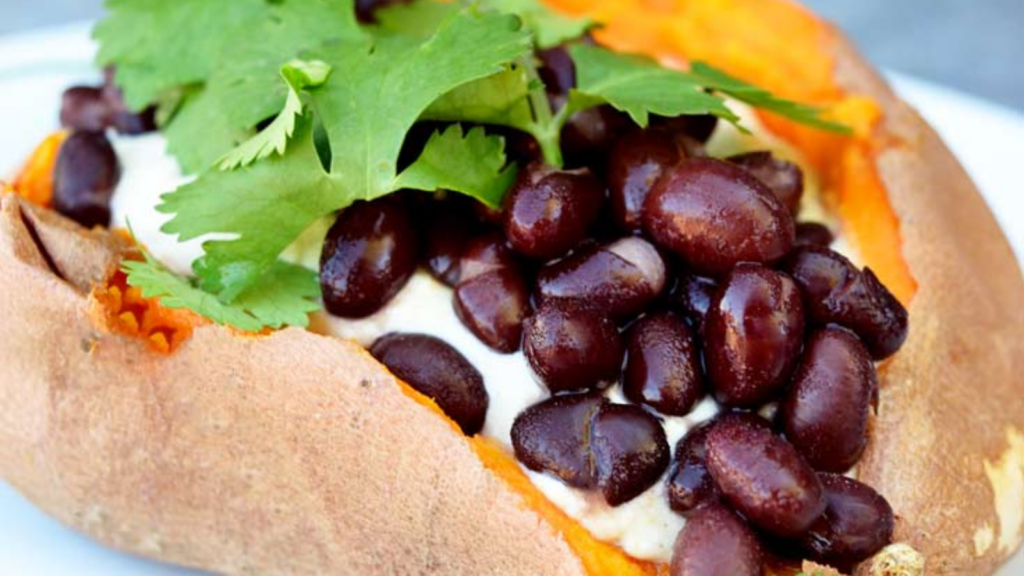 A single stuffed sweet potato sits on a white plate stuffed with hummus and black beans.