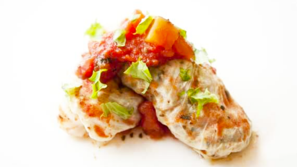 Two Italian cabbage rolls sit nestled together on a white surface.