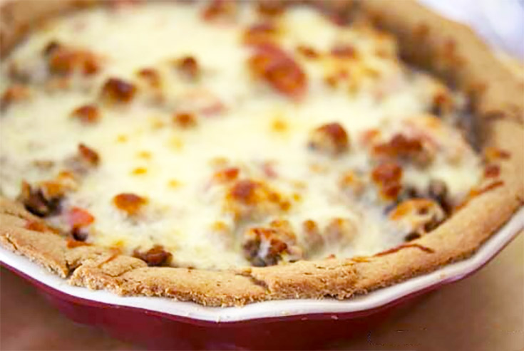 An Italian shepherds pie in a red pie pan. Melted cheese covered the entire surface of the pie filling.