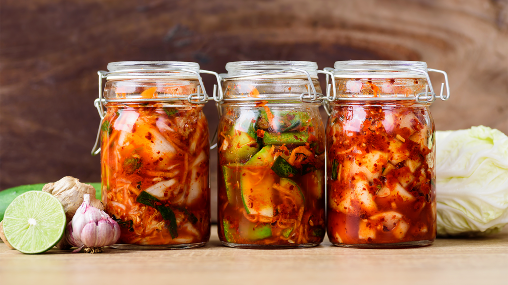 Three jars of kimchi on a wooden surface.