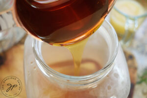 Adding honey to hot lavender water in a glass jug.