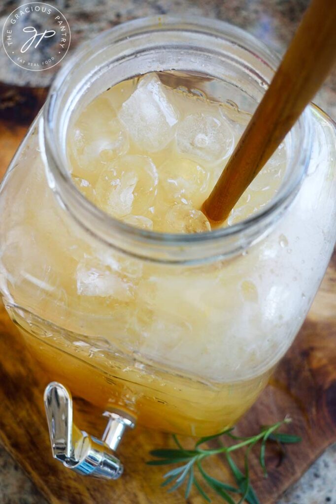 An overhead view of a glass jug with ice and lavender lemonade in it as well as a wooden spoon for stirring.