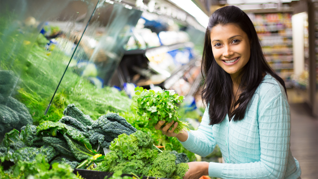 A woman in a grocery store holding a bunch of fresh herbs.