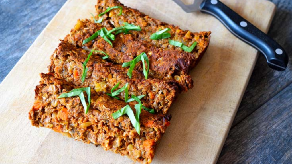 A side view of lentil loaf sliced on a cutting board and garnished with fresh greens.