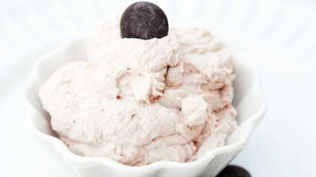 A white fluted bowl holds a serving of low carb chocolate mousse with a chocolate chip on top for garnish.