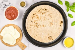 Pita bread placed on a baking dish with Margherita Pizza ingredients set around the dish.