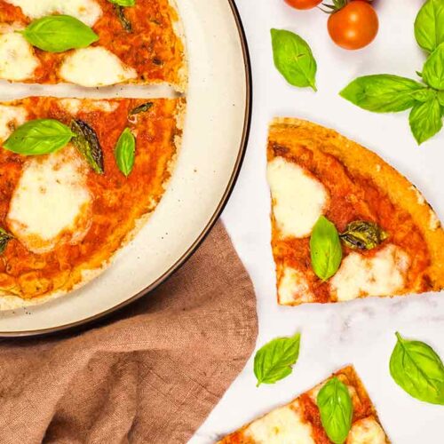 Two pieces of Margherita Pizza lay on a white surface next to a plate of the remaining pizza slices.