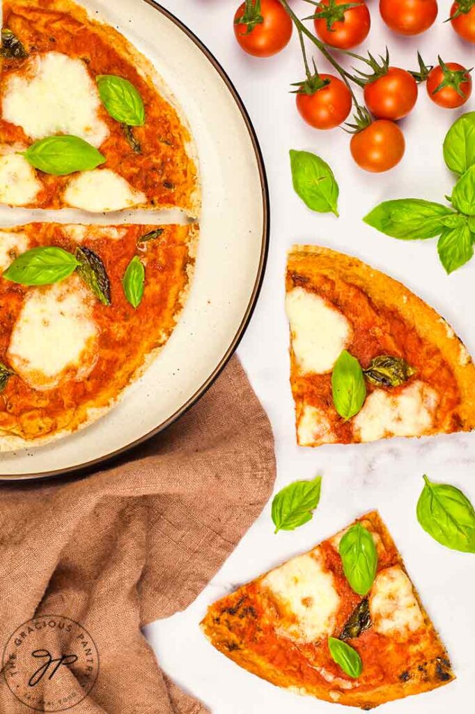 Two pieces of Margherita Pizza lay on a white surface next to a plate of the remaining pizza slices.