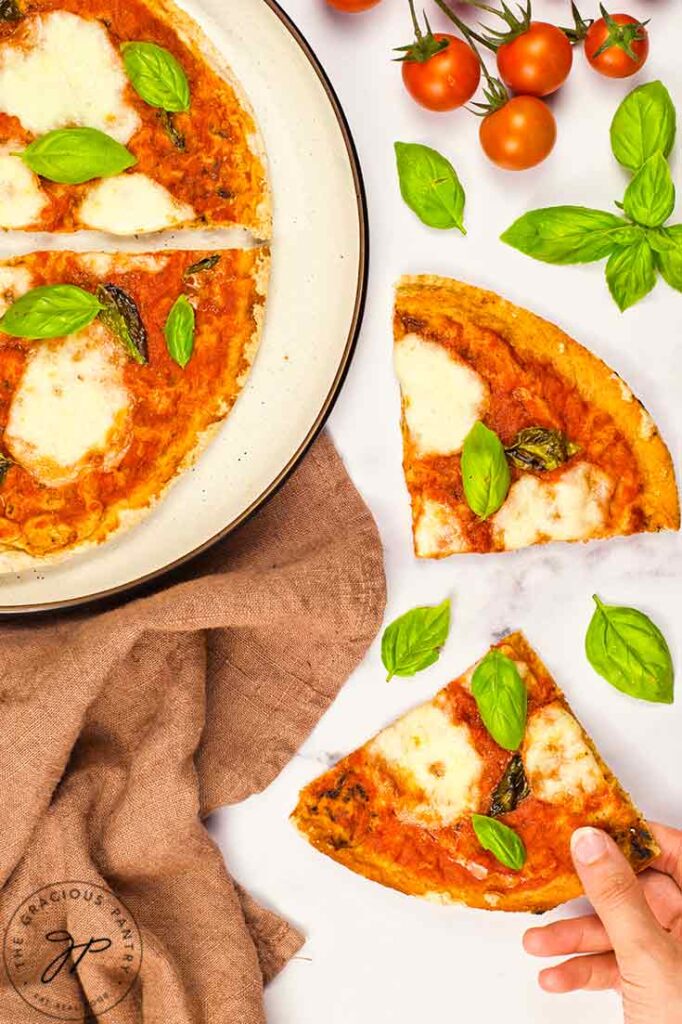 A hand reaches for a slice of Margherita Pizza from a white surface.