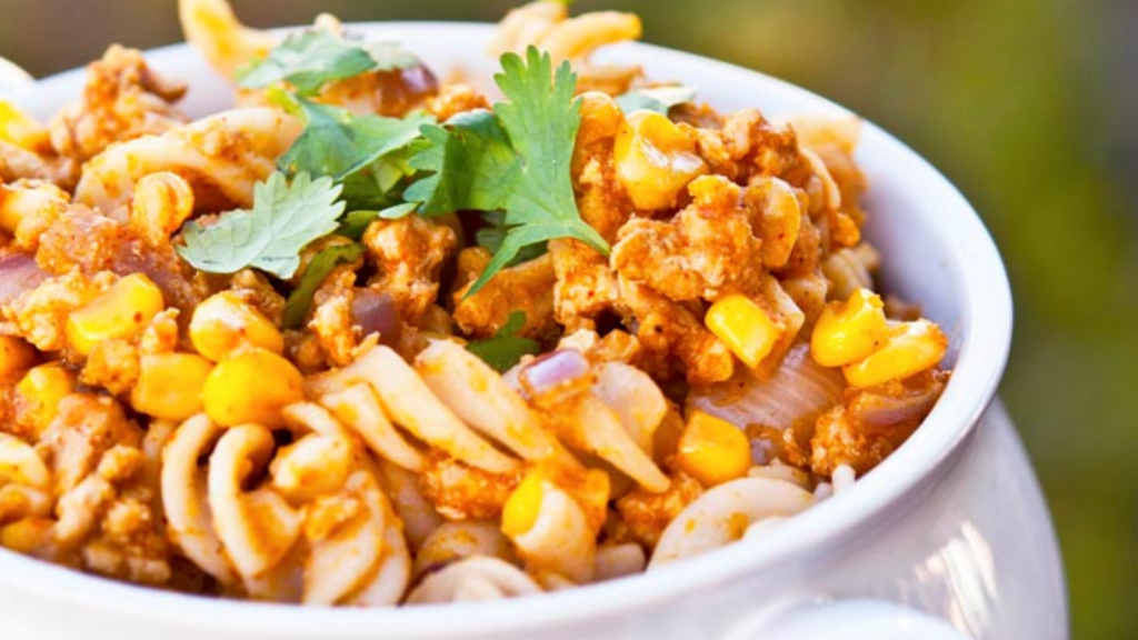 A white crock holds a serving of Mexican pumpkin rotini and is garnished with fresh parsley.