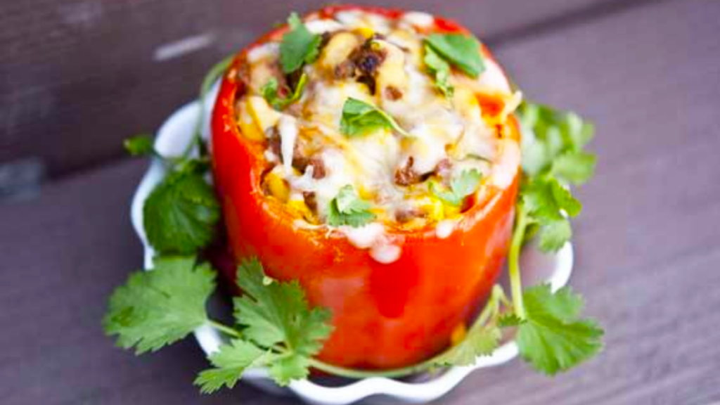 A single Mexican stuffed bell pepper sits in a white, fluted bowl with fresh cilantro for garnish.